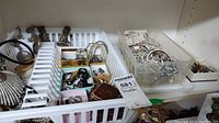 Wide shot of costume jewelry assortment in white plastic container and adjacent clear plastic container.