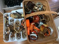 Overview of assorted costume jewelry in trays and baskets showing beadwork necklaces, bangles, and wristwatch.