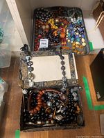 Overall view of two open fabric-covered boxes and one plastic bin containing multiple beadwork costume jewelry necklaces in assorted colors and styles