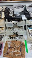 Wide shot of storage drawers and baskets filled with assorted pearl-like necklaces, bracelets, and brooches in various metallic tones and styles.