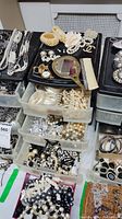 Overall view of plastic drawers and trays filled with assorted costume jewelry including necklaces, bracelets, bangles, earrings.
