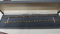Two yellow gold chains laid side by side in open gray case