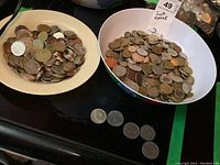 Two bowls filled with a variety of coins from multiple countries, shown from a top angle.