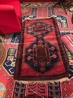 Wool rug with red background and blue geometric designs, showing overall front view with furniture surroundings.