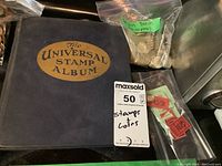 Photo showing front cover of The Universal Stamp Album with a bag of British pound coins and packing slips around it.