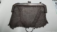 Front view of silver mesh purse with kiss-lock frame and chain strap draped over.