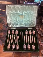 Full view of case interior showing twelve teaspoons and sugar tongs arranged in fitted slots