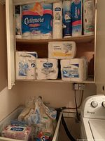 View of upper shelf stocked with multiple packages of Cashmere, Royale, and Compliments branded toilet paper, paper towels, and napkins.