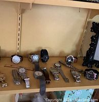 Wide view of shelf showing assortment of wristwatches and black ornate frame at right