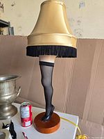 Front view of the deluxe leg lamp with gold shade and fishnet stocking leg on wooden base, showing the details and colors.