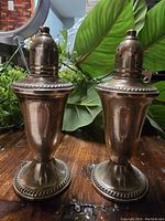 Two large antique sterling silver salt and pepper shakers with a visible patina, decorated bases and perforated tops placed on a wooden surface.