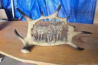 Full view of the carved wolves antler sculpture placed on a wooden surface with a blue tarp background.