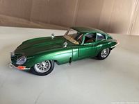 Side and front view of the green 1961 Jaguar E Type diecast model showing intact windshield, wire-spoke wheels, and detailed hood.