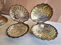 Two vintage silver plated scallop clam shell shaped butter dishes with lids open, showing inner glass inserts and scalloped design.