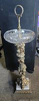 Full view of vintage standing ashtray showing crystal bowl, brass cherub stand, and marble base