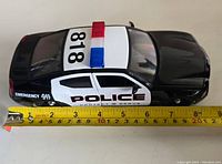Side view of black and white Dodge Charger police car model with measuring tape showing length approximately 8 inches.