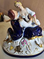 Porcelain figurine of a courting couple in royal blue and white with detailed gold trim and floral designs, showing front and side views.