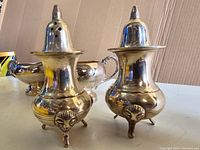 Two ornate silver salt and pepper shakers with round bodies and three-legged feet
