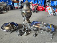 Overview of the lot showing the large samovar and various silverware pieces placed on the floor in a workshop or storage area.