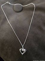 Full view of the sterling silver necklace with heart pendant on a black fabric background