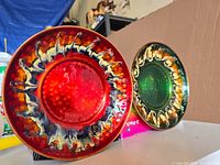 Oblique side view of the red and green enamel hammered copper bowls showing colorful swirling cream and brown rims, sitting on a surface indoors.