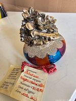 View of entire paperweight showing colorful multi-segmented art glass body with ornate silver floral top and certificate