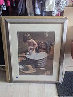 Framed print showing a young boy bathing in an aluminum tub with bubbles, accompanied by a dog, light wood frame with white mat, signed by Jim Daly.