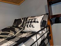 Twin bed with black metal frame featuring black and white checkered comforter and three accent pillows including deer and bear motifs.