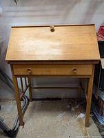 Front view of the closed wooden secretariat desk showing pull-down door and drawer with wooden knobs.