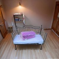 Day bed with mattresses wrapped in plastic on top, showing the metal frame design and condition.