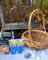 Wide shot showing all items arranged on a white surface outdoors, featuring a woven wicker basket, copper bandage box, packaged clippers, and other items.
