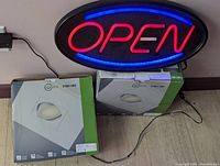 Photo of neon OPEN sign illuminated on the wall with two boxes of LED pot lights on the floor.