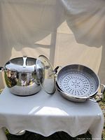 Photo showing the large saucepan with stainless steel lid alongside the perforated steamer insert with glass lid on white table.