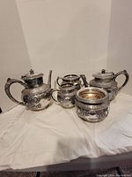 Silver-plated tea set with ornate floral designs, consisting of teapot, creamer, sugar bowl, and spoon bowl