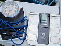 Manual analog floor scale with dial and black base, digital scale with metal foot pads and LCD screen, and blue skipping rope with black handles placed on a white surface