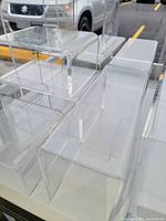 Close-up photo of various sizes of clear acrylic slatwall display shelves stacked together.