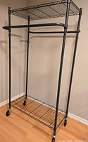 Fully assembled oval clothing rack with two tiers, double hanging bars, wire mesh shelves on top and bottom, and caster wheels.