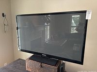 Front view of Samsung plasma TV mounted on TV stand, screen off, reflecting room interior.