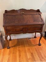 Front view of closed desk showing drop-front panel with burl veneer and two lower drawers