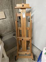 Front view of assembled wooden easel showing full H-frame, top clamp, lower tray and rear wheels