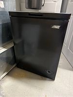 Front view of a black Arctic King chest freezer showing the brand label and control dial.