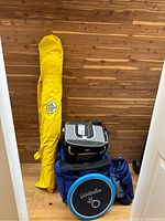 Photo shows the yellow beach umbrella in its carrying bag standing upright with the two coolers and frisbee packed together on a wooden floor.