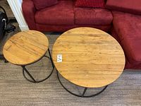 Two round tables next to a red sofa, larger coffee table on right, smaller side table on left, showing wood tops and black metal bases.