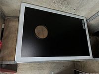 Top-down photo of one black cornhole board with metal frame and circular hole
