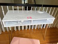 White marble-effect desk with gold legs and open storage compartments underneath, shown from front