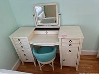 Front view of white makeup desk with drawers and attached mirror, turquoise swivel chair in front.