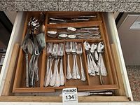 Full top-down view of bamboo drawer organizer with flatware neatly arranged in compartments including forks, spoons, serving utensils, and knives.