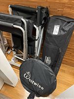 Photo showing two black metal frame directors chairs, a black Kamprite bag, and a black Wolfwise circular bag all neatly placed on a wooden floor.