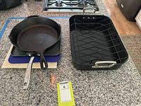 Cookware items including cast iron skillet, roasting pan with rack, and bakeware trays on a kitchen countertop.