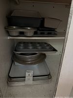 Stacked collection of various baking pans including muffin pans, cake pans, and multiple baking sheets.